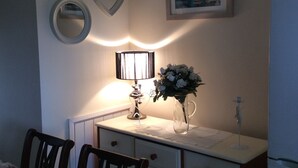 A compact kitchen with a white countertop, a vase with flowers, a framed picture, and a refrigerator.