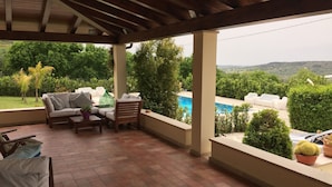 A covered patio with a pool, outdoor furniture, and a view of the landscape.