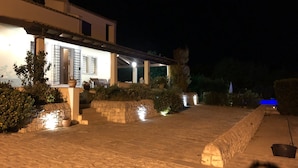 A nighttime view of a house with a stone pathway leading to a covered patio area.