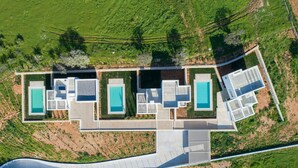 Vista aerea di una casa moderna con tre piscine, un vialetto lastricato e vegetazione circostante.