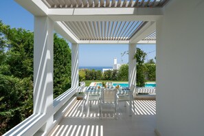 A covered outdoor seating area with a view of a swimming pool and the sea. - Basilico villa,Relaxation in luxury,seaview&private pool,near beach&all you need (PANORMOS RETHYMNO CRETE GREECE)