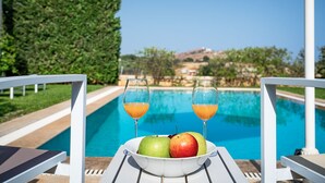 Un tavolo a bordo piscina con una ciotola di frutta e due bicchieri di succo d'arancia, con vista su una piscina e un panorama.