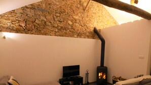 Ett mysigt vardagsrum med ett tak av natursten, en öppen spis, en tv och en soffa.