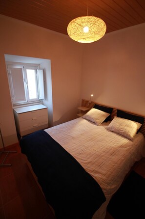 A bedroom with a bed, a dresser, a window, and a hanging light fixture.