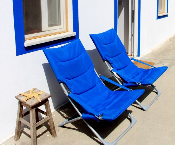Two blue lounge chairs with metal frames, a small wooden stool, and a starfish decoration on the stool.