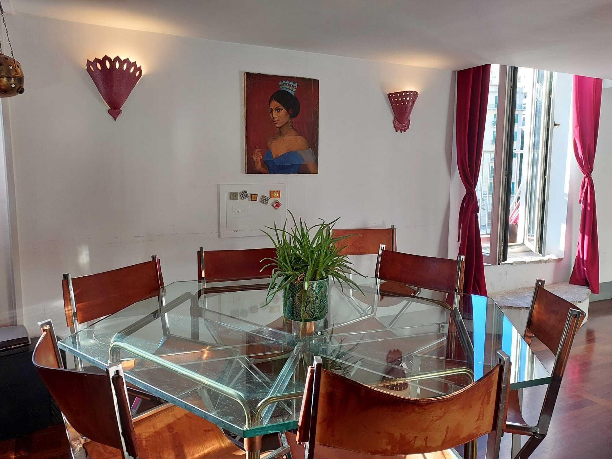 Un comedor con una mesa de vidrio rodeada de sillas de madera, una planta en maceta y un cuadro colgado en la pared.