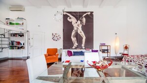 A modern living room with a glass coffee table, a white sofa, an orange armchair, and a large abstract painting on the wall. - Naples Mergellina with charm  (Napoli)