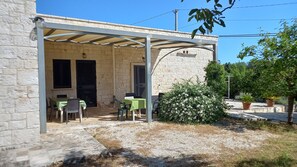 Ein Steinhaus mit überdachter Terrasse, Sitzgelegenheiten im Freien und einem kleinen Garten.