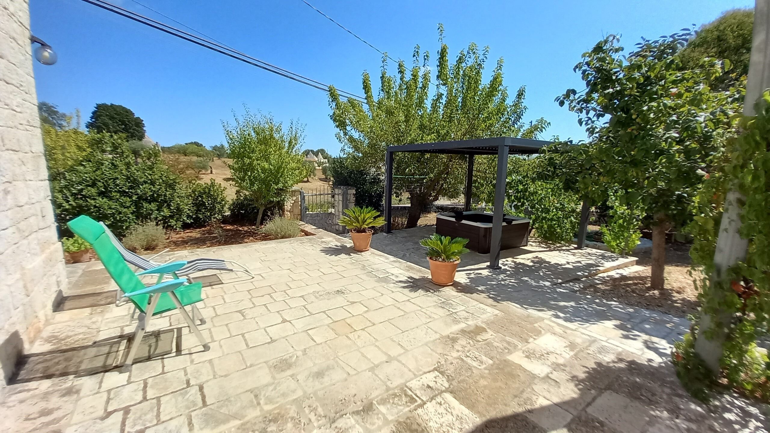 A patio with a pergola, potted plants, and a green chair.