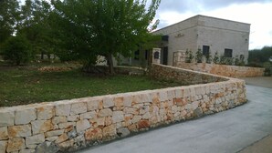 A stone retaining wall with a grassy area and a building in the background. - Authentic Stone Villa with Hot Tub | Valle d'Itria View | Near Alberobello & Sea (Locorotondo)