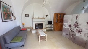 A living room with a grey sofa, a small table, a fireplace, a TV on a stand, and a wooden cabinet. - Authentic Stone Villa with Hot Tub | Valle d'Itria View | Near Alberobello & Sea (Locorotondo)