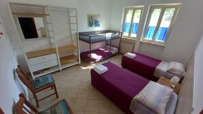 Ein Schlafsaalzimmer mit Stockbetten, einem Schreibtisch, einem Stuhl und einem Fenster mit Vorhängen.