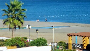 Uma praia com palmeira, poste de luz e um prédio de fachada amarela.