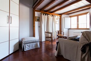 A room with wooden beams, a white wardrobe, a cushioned bench, a wooden chair, and a bed with a blanket.