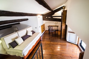 Une chambre à coucher confortable, aménagée en mezzanine, avec des poutres apparentes, un canapé-lit, une table à manger et une petite fenêtre.