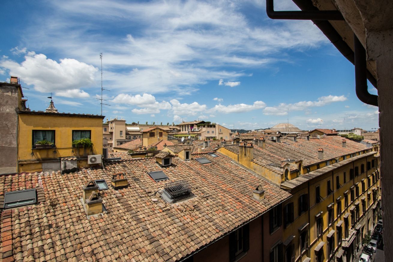 A rooftop view of a densely packed urban area with terracotta-tiled roofs and yellow buildings.
