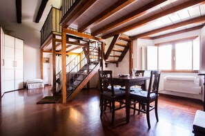 A spacious room with a wooden staircase, a dining table with chairs, and a large window providing natural light. - ALTIERI LOFT PANTHEON (Roma)