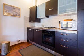 A compact kitchen with dark cabinets, a gas stove, an oven, and a microwave. - ALTIERI LOFT PANTHEON (Roma)