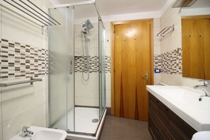 A modern bathroom with a glass shower enclosure, a wooden door, and a white sink with a mirror.