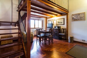 A wooden staircase leading to a loft area with a dining table and chairs, a television, and a framed picture on the wall.