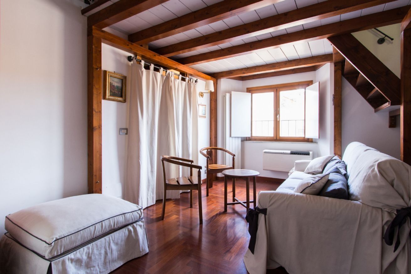 A cozy room with a wooden ceiling, a sofa, a chair, a small table, and a window with curtains.