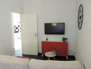 A modern living room with a flat-screen TV mounted on the wall, a red cabinet below it, and a small round table with a cactus.