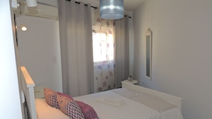 Un dormitorio con cama, mesita de noche, lámpara y ventana con cortinas.
