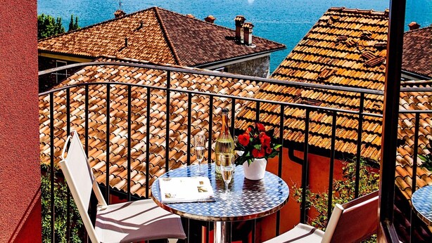 A terrace with a table set for two, overlooking a lake with mountains in the background.