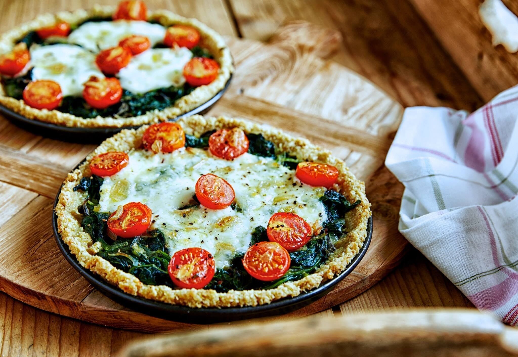 Two quiches on a wooden board with a cloth napkin beside them.