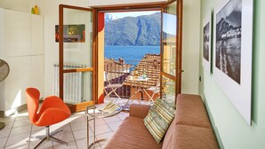A balcony with a view of a lake and mountains, a sofa, a chair, and a table with a bottle and glasses.