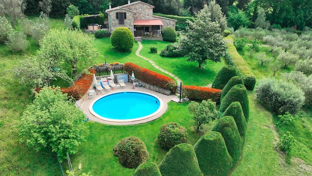 Un jardin privé avec une piscine, entouré de haies bien entretenues et d’une maison en pierre.