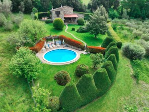 Un jardin privé avec une piscine, entouré de haies bien entretenues et d’une maison en pierre.