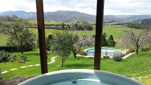 Un bain à remous avec vue sur une piscine et un jardin agrémenté d’arbres et d’une pelouse.