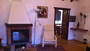 Ein Wohnzimmer mit Kamin, einem Sessel, einer Lampe und einem Gemälde an der Wand.