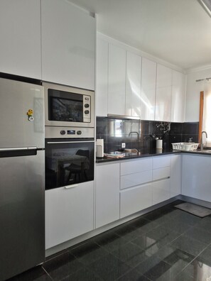 A modern kitchen with stainless steel appliances, white cabinetry, and a black countertop.
