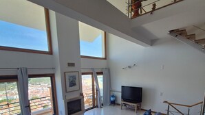 Ein geräumiges Wohnzimmer mit einem Ecksofa, einem Flachbildfernseher und einem Balkon mit Blick auf die Stadt.