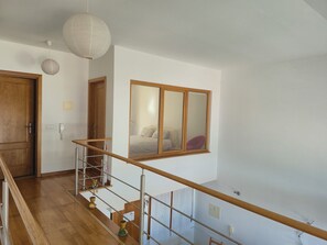 A staircase with a wooden handrail, a wooden door, and a large mirror reflecting a bed and a red chair.