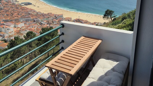 Ein Balkon mit Holztisch und gepolstertem Sitz einer Küstenstadt überblickend.