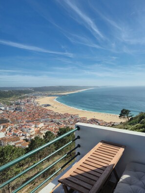 A seaside view from a balcony with a wooden bench, overlooking a beach and a coastal town.