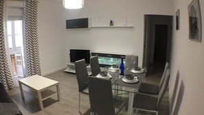 Un comedor moderno con una mesa de vidrio dispuesta para cuatro personas, sillas grises, un televisor de pantalla plana y un mueble blanco sobre el televisor.