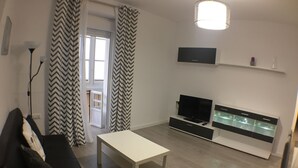 Una sala de estar moderna con un sofá negro, una mesa de centro blanca, un televisor de pantalla plana y un aparador.