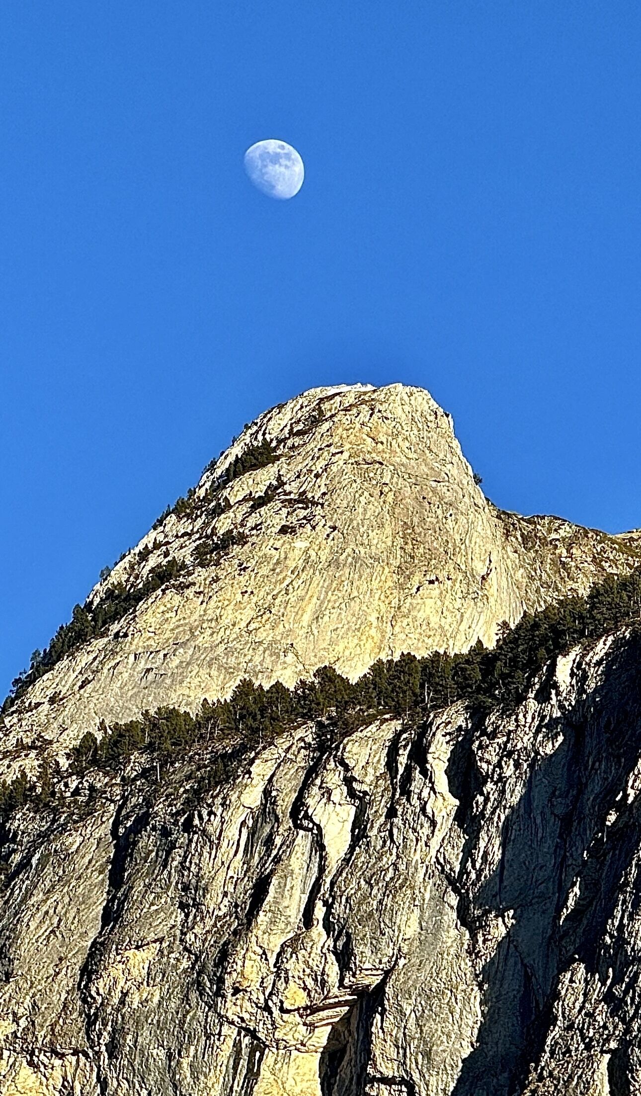 A mountain with a prominent peak and a visible moon in the sky.