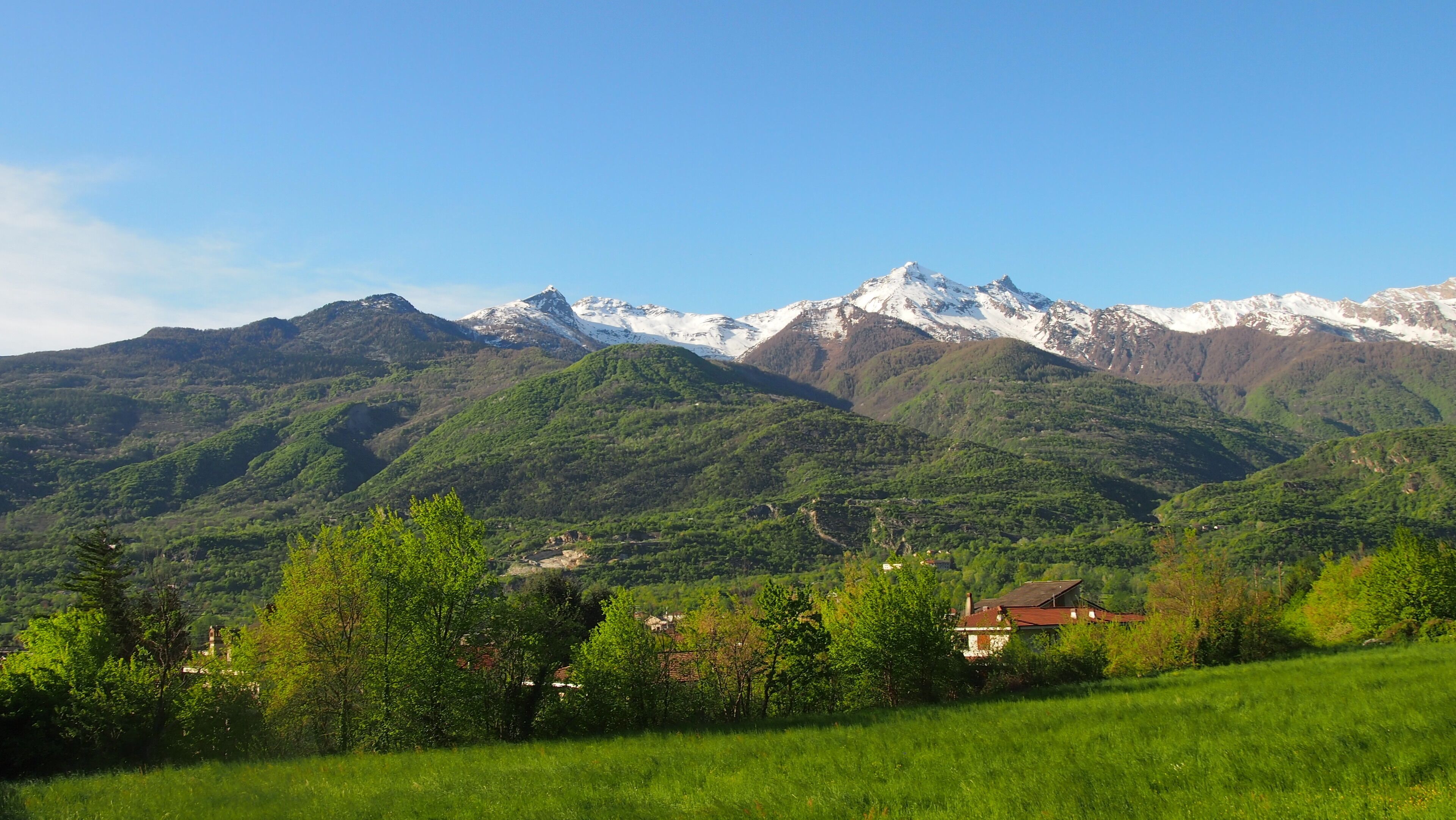 A mountainous landscape with snow-capped peaks and a valley with green fields and houses.