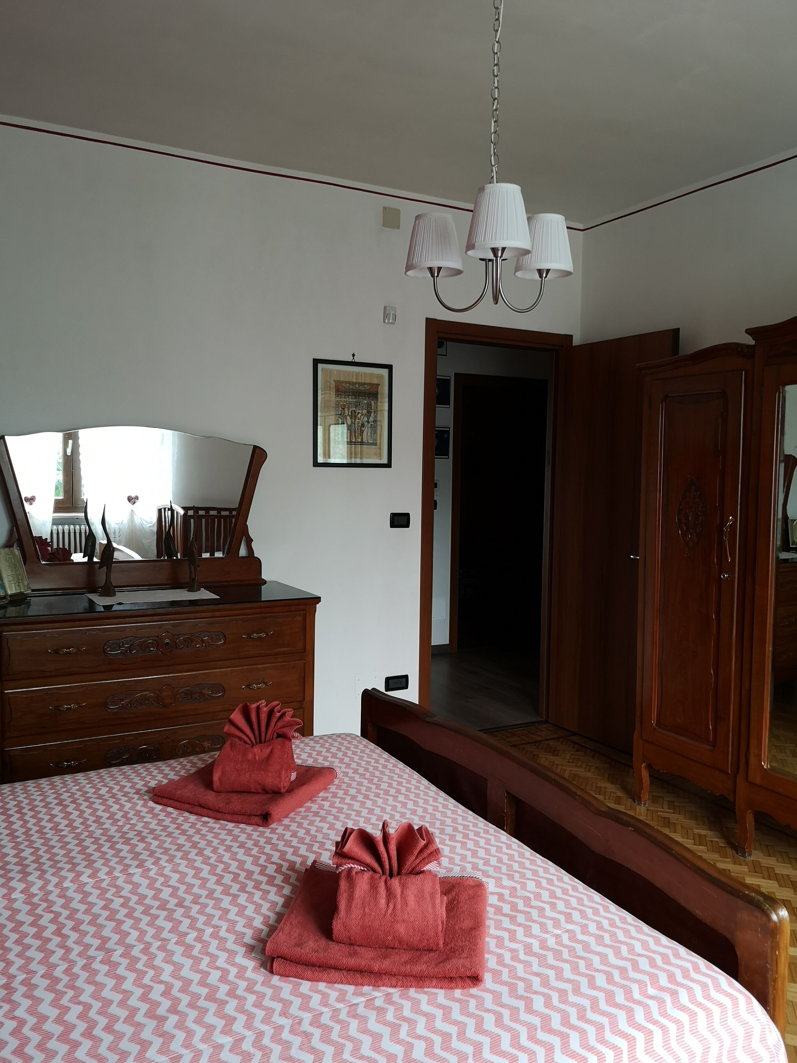 A bedroom with a bed, a dresser, a mirror, and a chandelier.