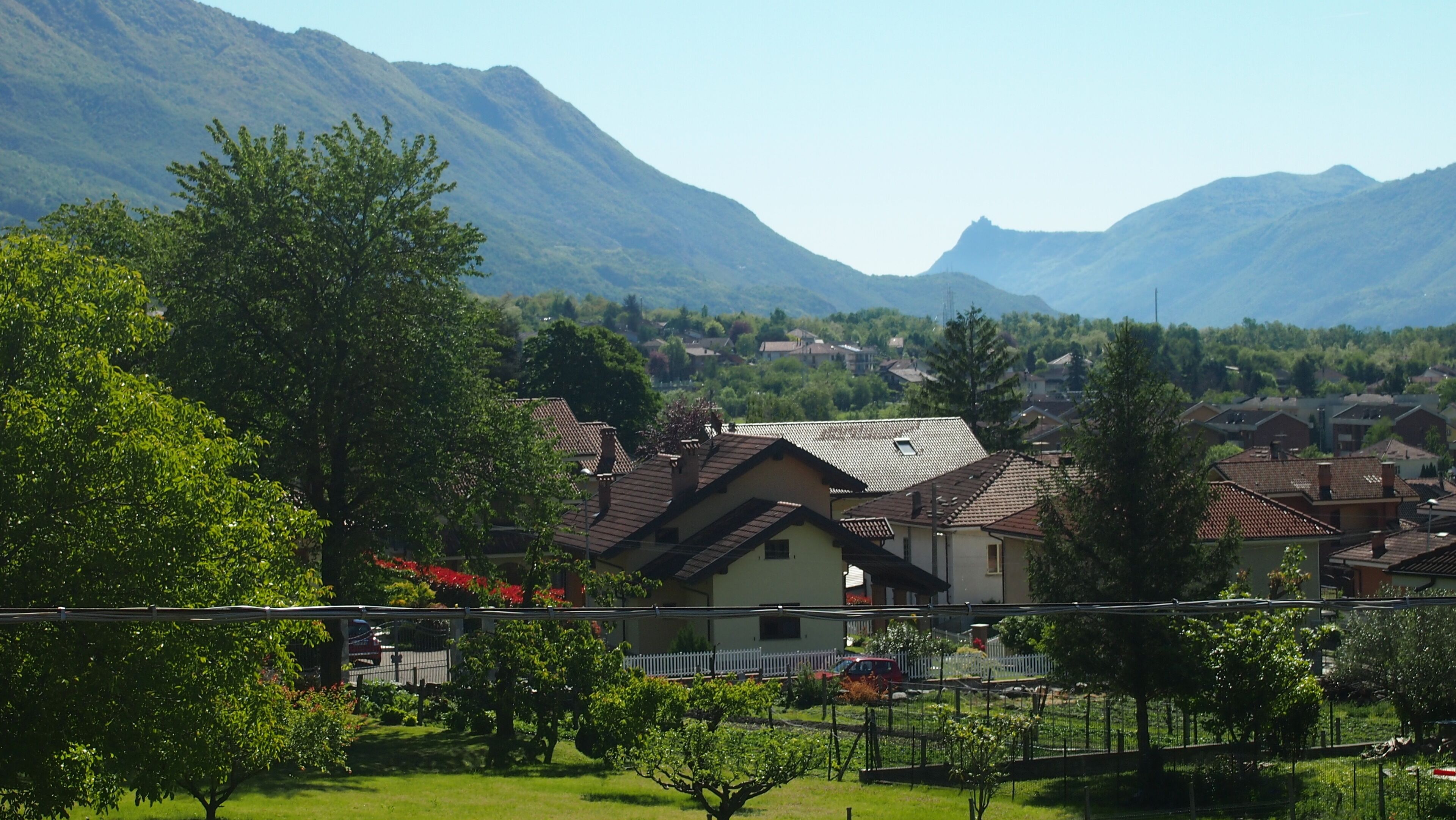 A residential area with houses, a fenced garden, and mountains in the background.