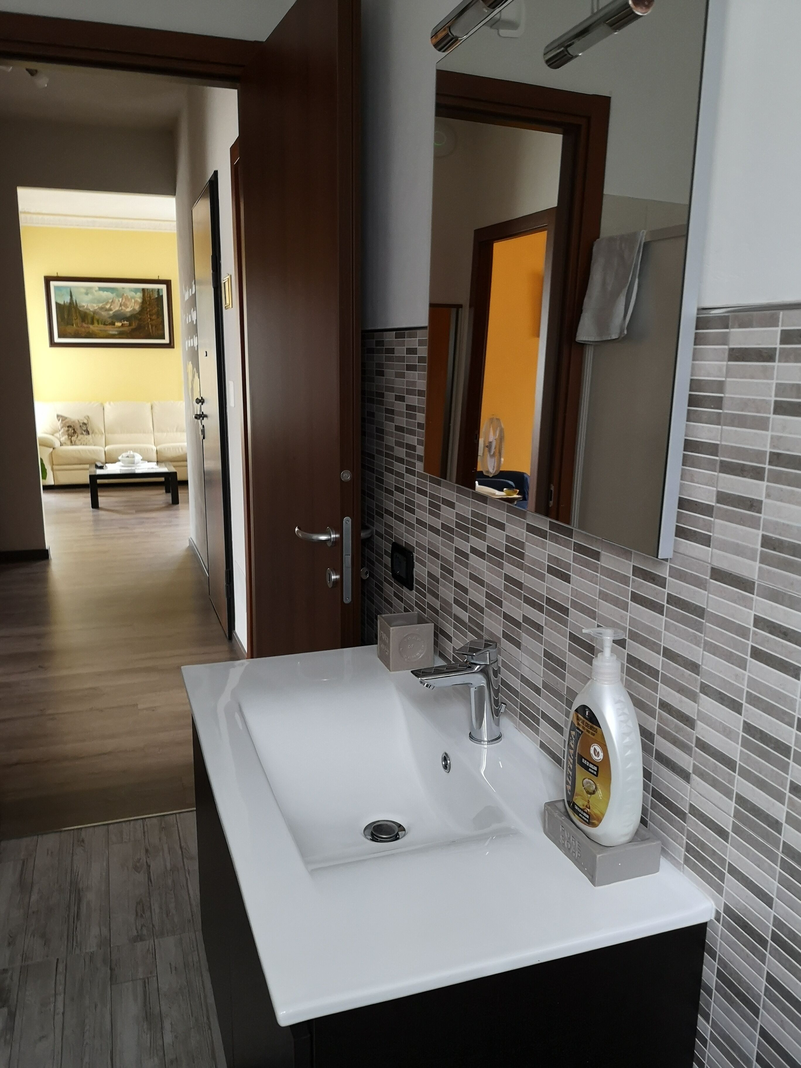 Un bagno moderno con un lavandino bianco, uno specchio e una bottiglia di sapone per le mani.