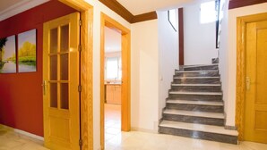 A staircase with marble steps leading to a second floor, adjacent to a wooden door and a red wall with two landscape paintings. - Beautiful house in Granada just 10min from the center + (PARKING IN THE CENTER) + WIFI (Ambroz)