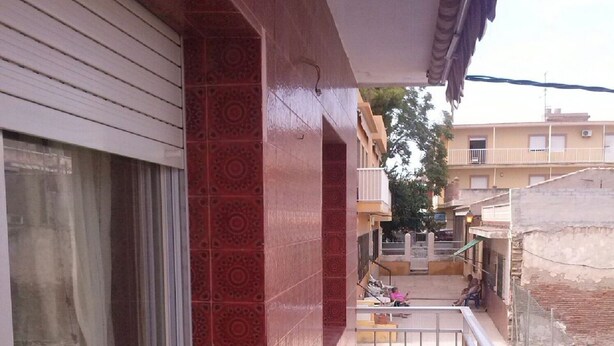 A narrow balcony with patterned tiles, a window with curtains, and a view of a residential area with buildings and a tree. - Taibilla floor (Los Nietos) (Los Nietos)
