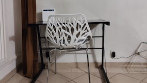 Ein Zimmer mit einem weißen Stuhl, einem Schreibtisch mit Computer und einem Wandbild von einem Wald.