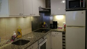 Eine kleine Küche mit weißen Schränken, einer Arbeitsplatte aus Granit, einer Spüle aus Edelstahl, einer Mikrowelle und einem Kühlschrank.